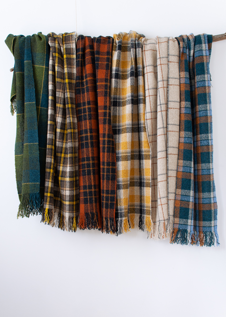 The checkmate scarf collection handwoven by Victoria Pemberton. Six scarves in different check designs hang on a Eucalyptus branch against a white background.