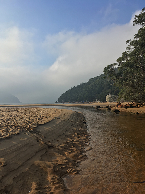 A stunning beach on a sunny autumn day, with blue skies and a tidal stream.