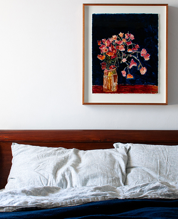 An ink painting of strawflowers against an indigo background hangs above an antique sleigh bed. The bed has a hand dyed and handwoven indigo throw draped across the end.